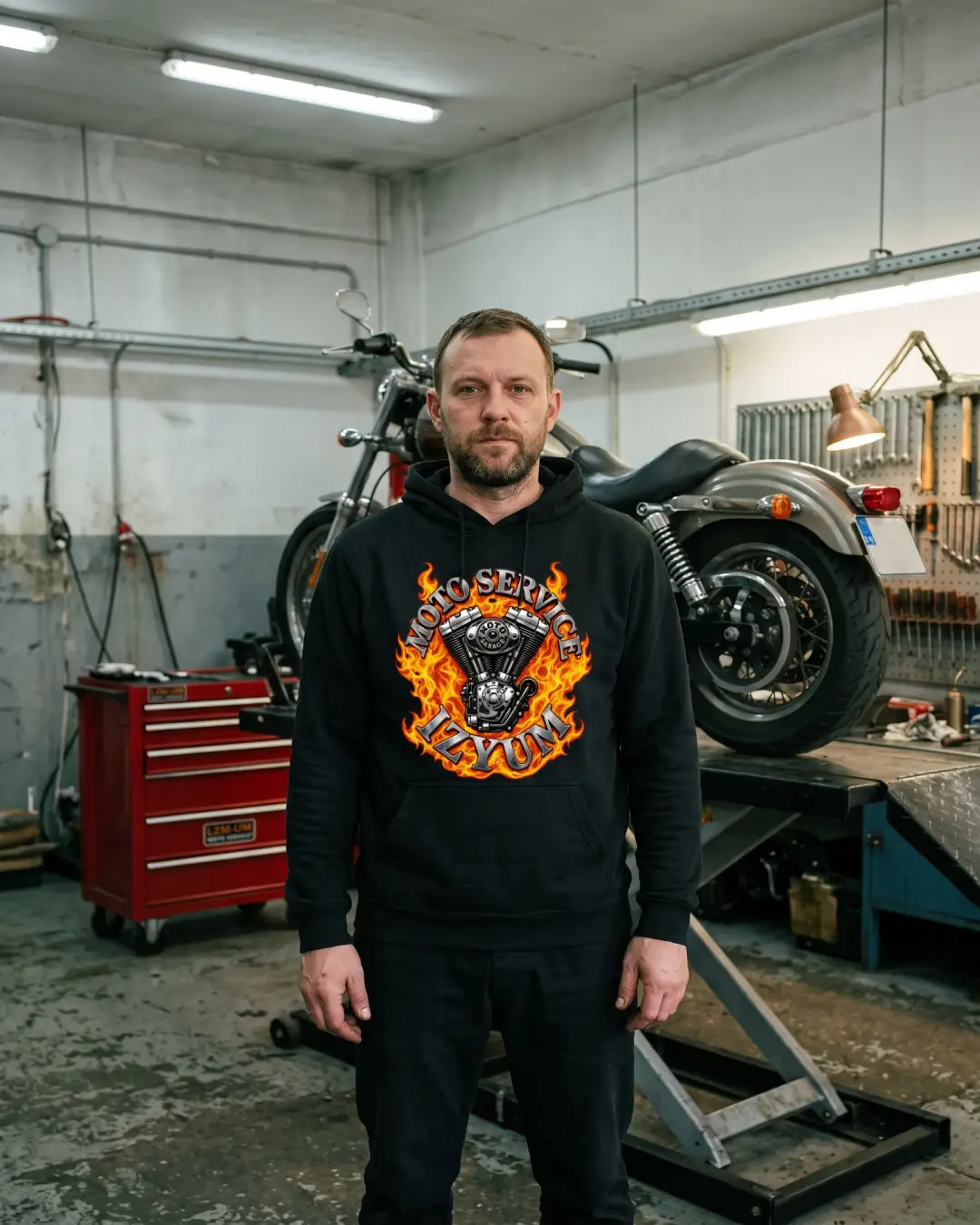 Механік у худі Moto Service Izyum у майстерні поруч з мотоциклом